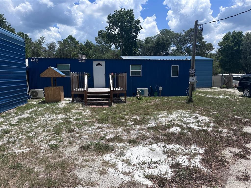 A blue metal-sided mobile home features a wooden front porch and a small wishing well — 45506 MAGNOLIA STREET, PAISLEY, FL