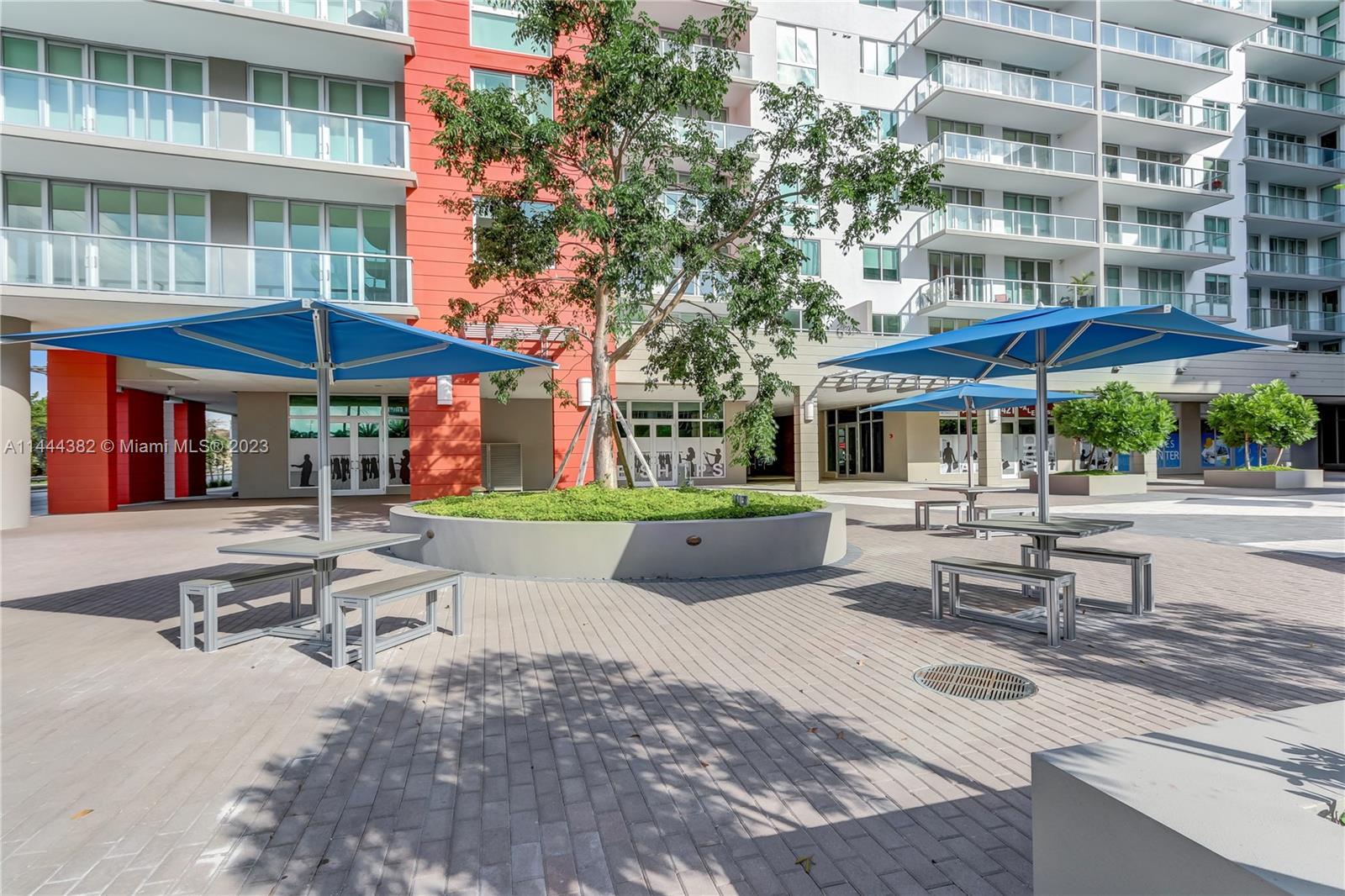 An outdoor courtyard features blue patio umbrellas, metal tables, and a central circular planter — 7825 NW 107th Ave # 816, Doral FL 33178, DORAL, FL