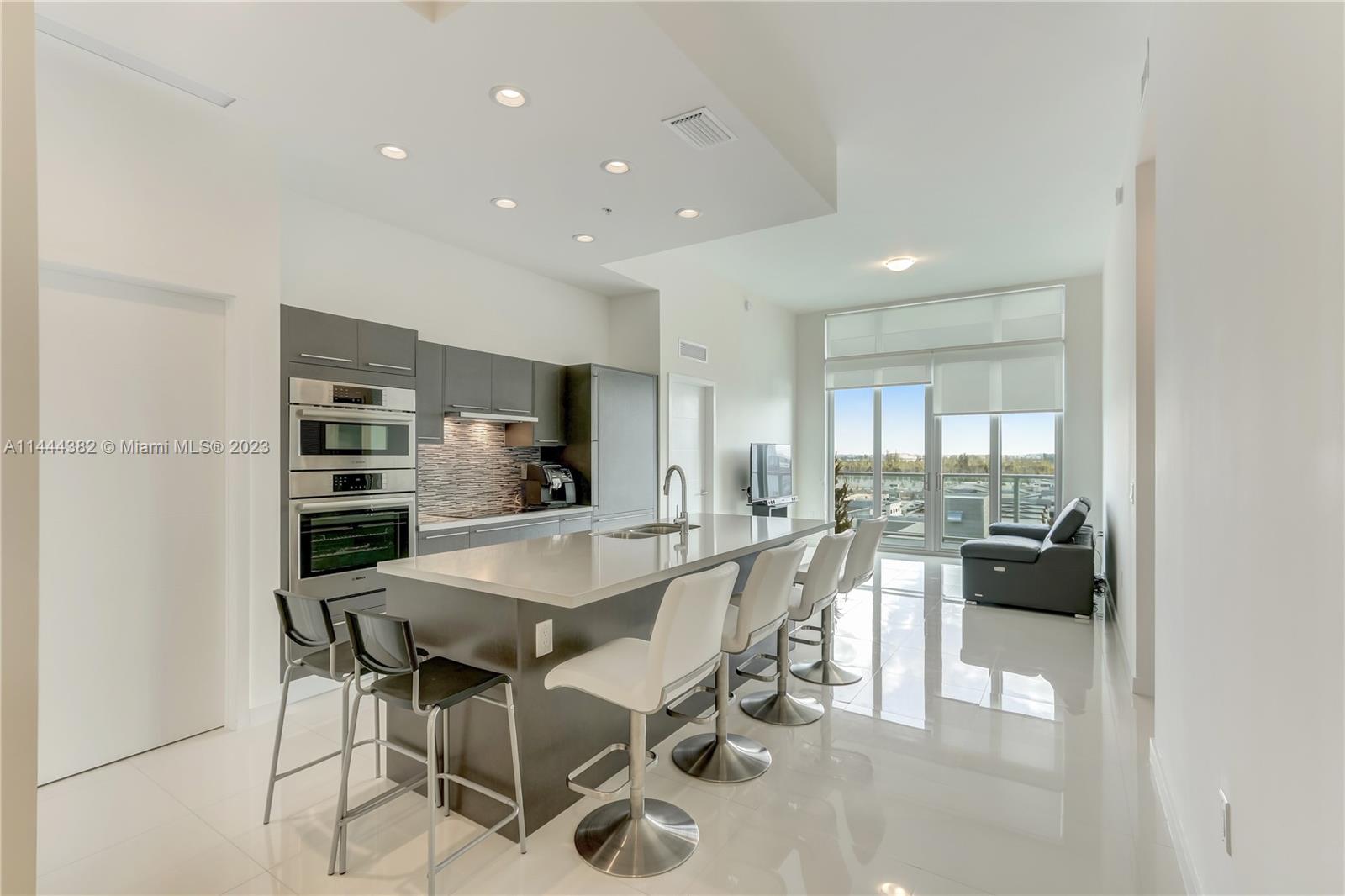 A modern kitchen features a large island, white bar stools, and gray cabinetry — 7825 NW 107th Ave # 816, Doral FL 33178, DORAL, FL
