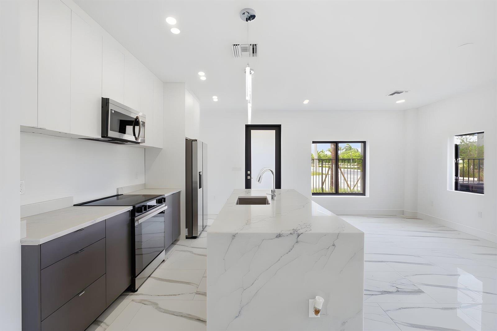 A modern kitchen features white cabinetry, a marble-topped island, stainless appliances, and white tile flooring — 1548 NW 1st Avenue, Pompano Beach FL 33060, POMPANO BEACH, FL