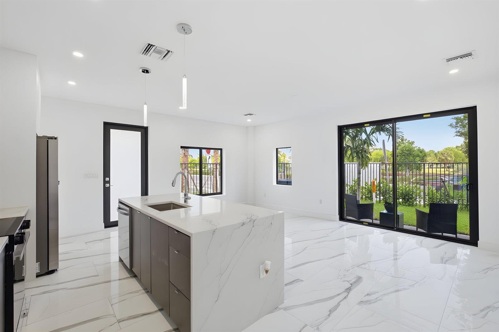 A modern kitchen features a marble-topped island, gray cabinetry, and sliding glass doors to a yard — 1548 NW 1st Avenue, Pompano Beach FL 33060, POMPANO BEACH, FL