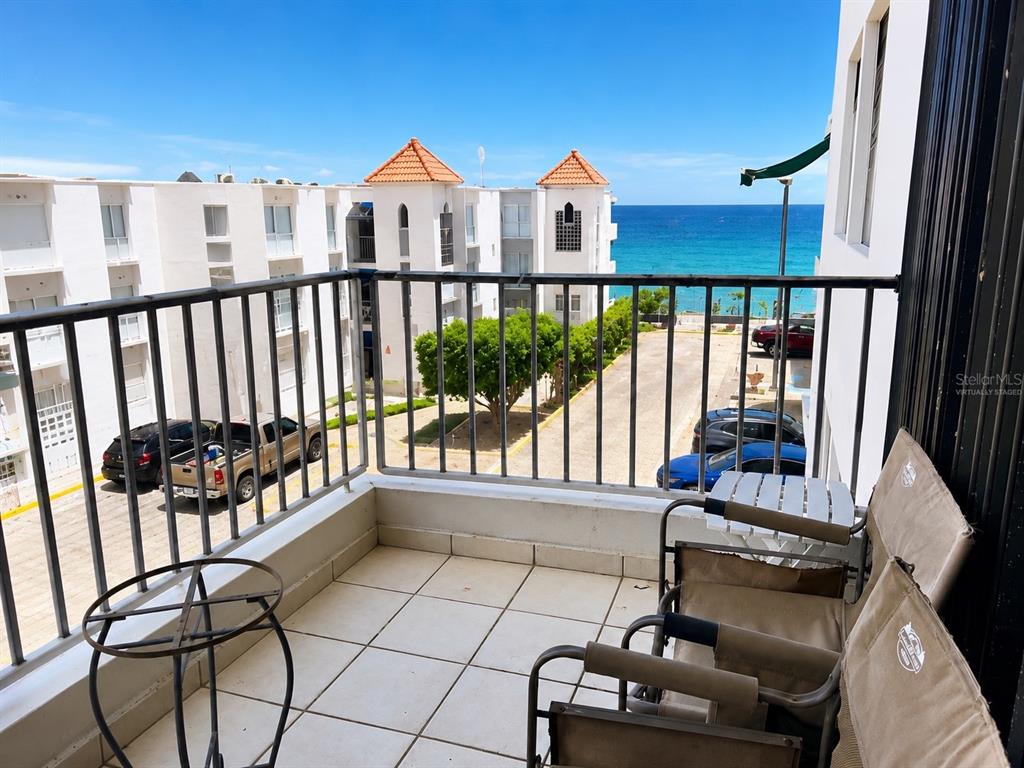 A balcony with tiled flooring, metal railings, and patio furniture overlooks a parking lot and ocean — 3444 VICTORIA DEL MAR UNIT 3-A, RINCON, PR