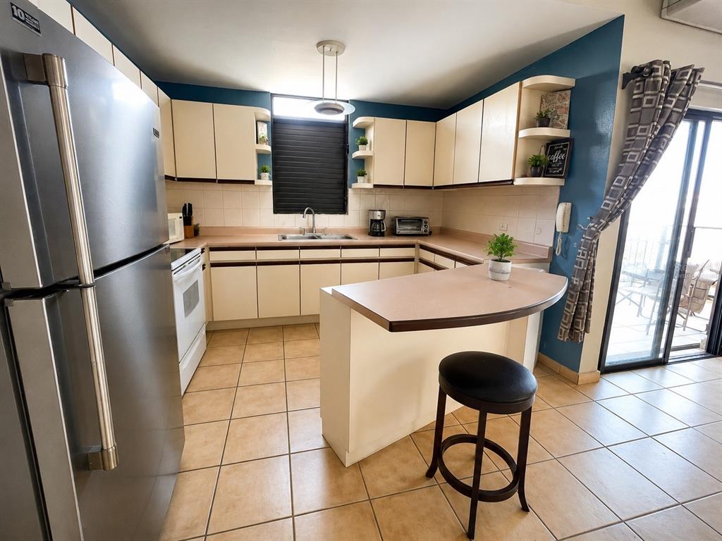 A kitchen features light-colored cabinets, a stainless steel refrigerator, tile flooring, and a breakfast bar — 3444 VICTORIA DEL MAR UNIT 3-A, RINCON, PR