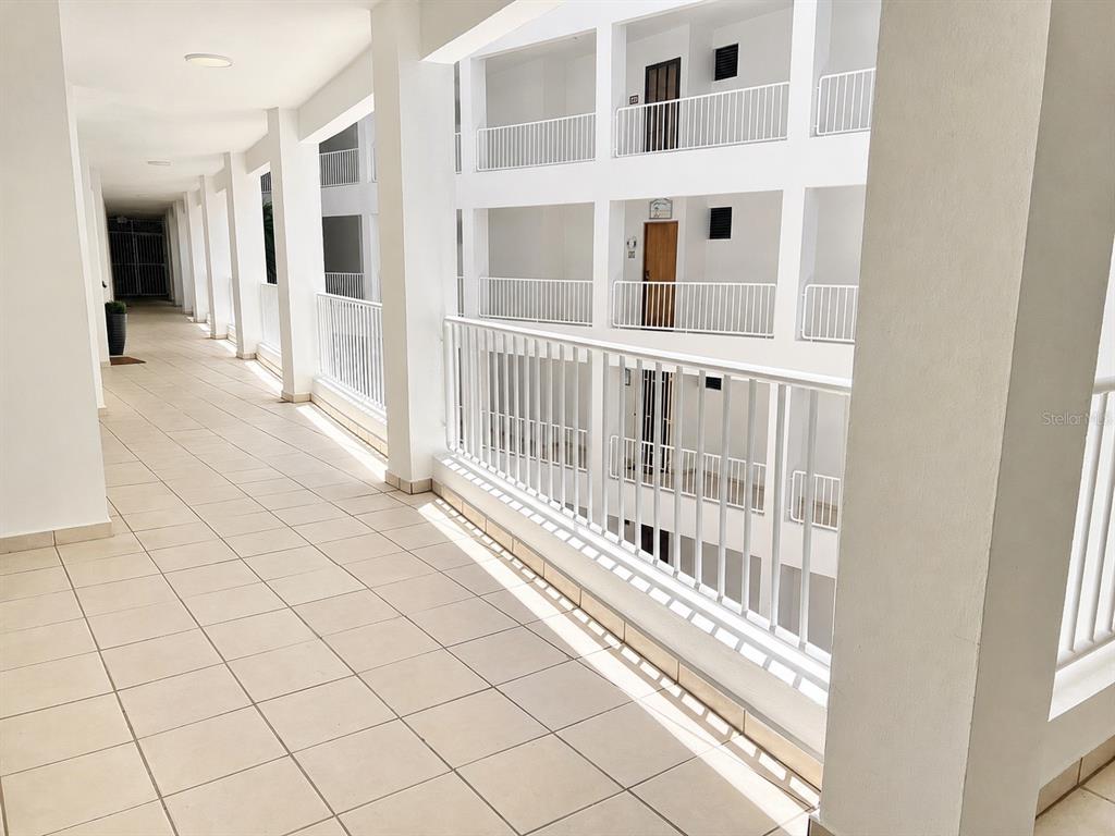 An outdoor apartment building corridor features white railings, tiled floors, and multiple levels — 3444 VICTORIA DEL MAR UNIT 3-A, RINCON, PR