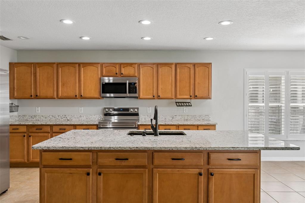 A kitchen features wooden cabinets, granite countertops, a central island, and stainless steel appliances — 14759 ROYAL POINCIANA DRIVE, ORLANDO, FL