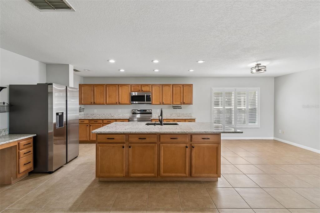 A kitchen features wood cabinets, granite countertops, a central island, and stainless steel appliances — 14759 ROYAL POINCIANA DRIVE, ORLANDO, FL