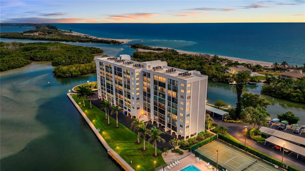 An aerial view shows a multi-story apartment building situated on a waterfront lot with tennis courts — 9397 MIDNIGHT PASS ROAD UNIT 903, SARASOTA, FL