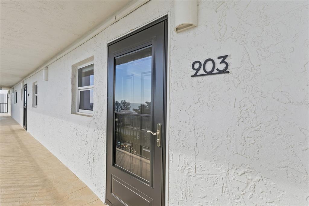 An exterior view of a building hallway showing a dark door labeled 903 — 9397 MIDNIGHT PASS ROAD UNIT 903, SARASOTA, FL