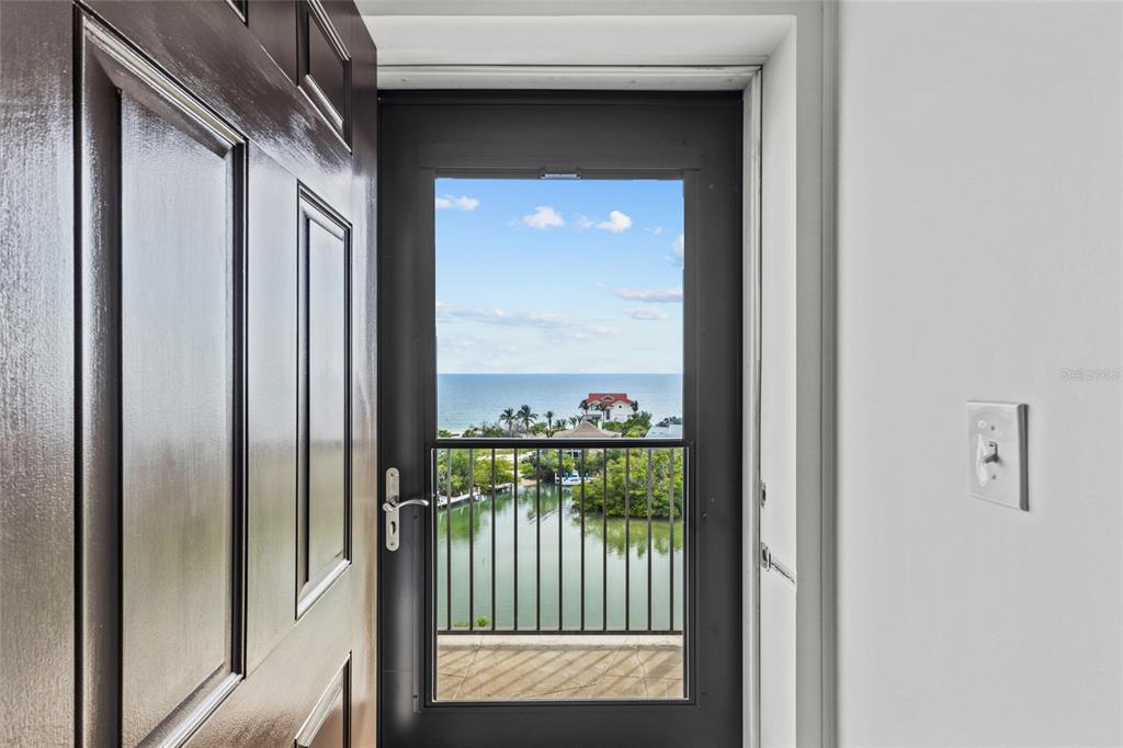 An open dark brown door reveals a balcony overlooking a canal and the ocean — 9397 MIDNIGHT PASS ROAD UNIT 903, SARASOTA, FL