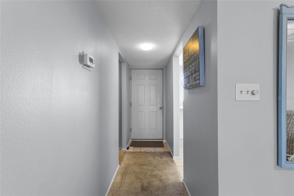 A hallway with light gray walls, carpeted flooring, and a white door at the end — 9397 MIDNIGHT PASS ROAD UNIT 903, SARASOTA, FL