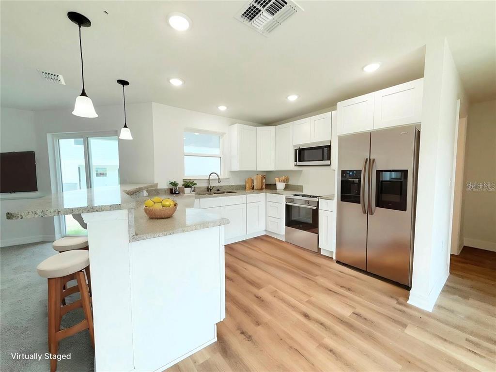 A kitchen features white cabinets, stainless steel appliances, a granite island, and wood-look flooring — 222 CARPENTERS WAY UNIT 67, LAKELAND, FL