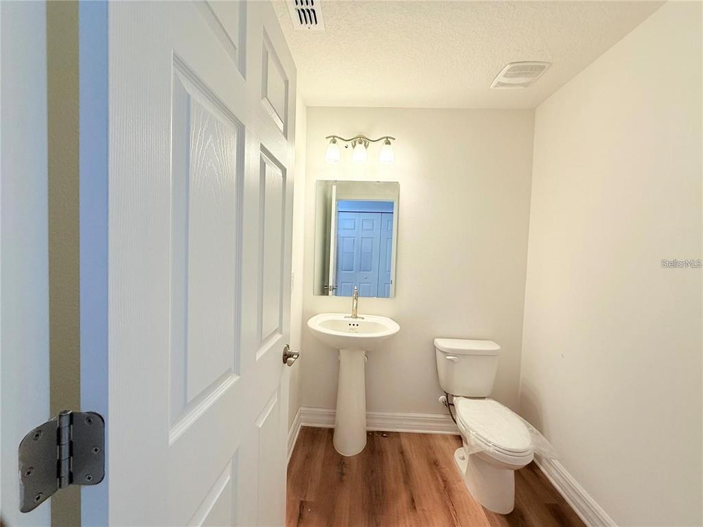 A small bathroom features a pedestal sink, a toilet, and light wood-look flooring — 222 CARPENTERS WAY UNIT 67, LAKELAND, FL