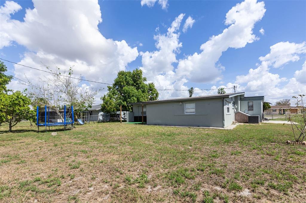 The exterior of a gray single-story house features a large backyard with a blue trampoline — 3425 HARBOR BOULEVARD, PORT CHARLOTTE, FL