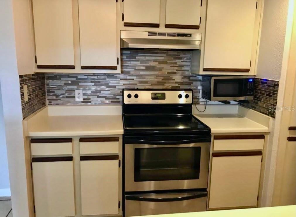 A kitchen features white cabinets, stainless steel appliances, and a multi-colored glass tile backsplash — 4460 PERKINSHIRE LANE UNIT T206, ORLANDO, FL