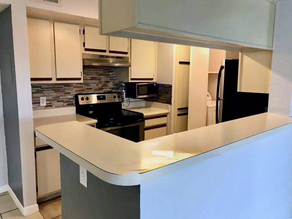 A kitchen features white cabinets, a black stove, a tile backsplash, and a breakfast bar — 4460 PERKINSHIRE LANE UNIT T206, ORLANDO, FL