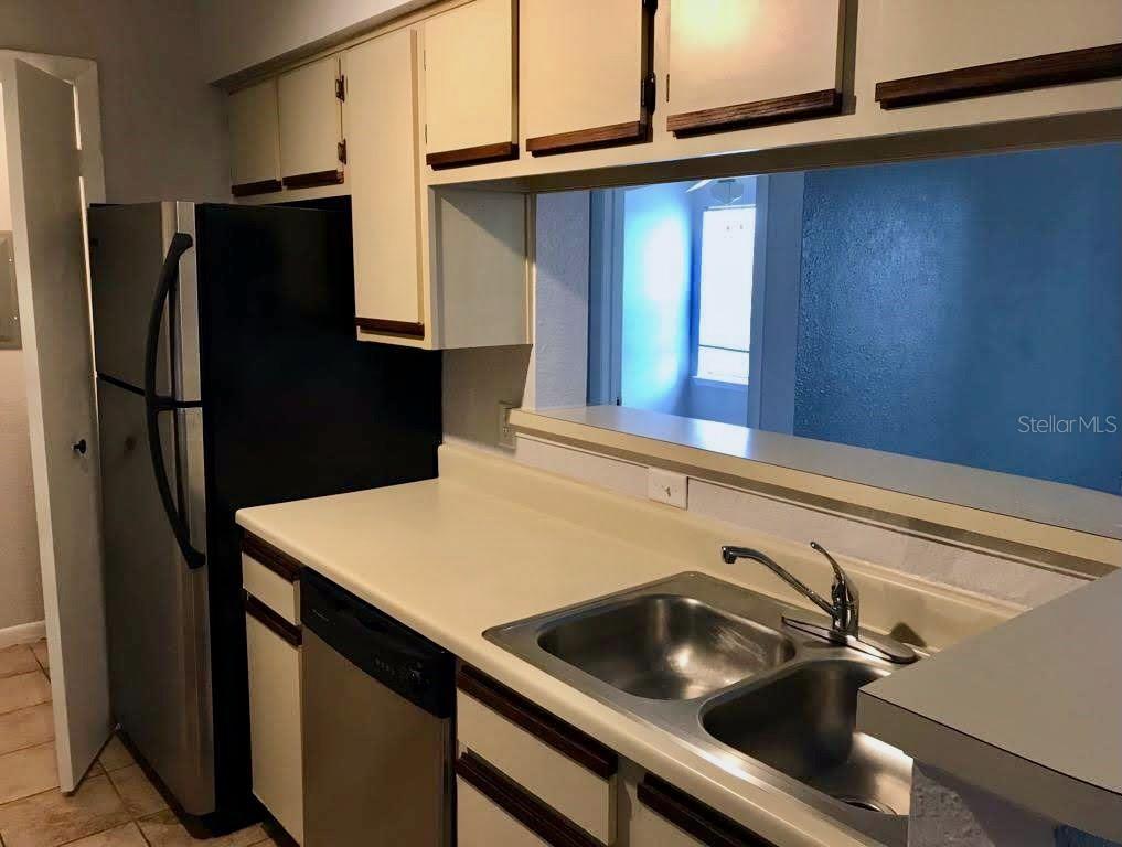 A kitchen features white cabinets, stainless steel appliances, a double sink, and a pass-through window — 4460 PERKINSHIRE LANE UNIT T206, ORLANDO, FL