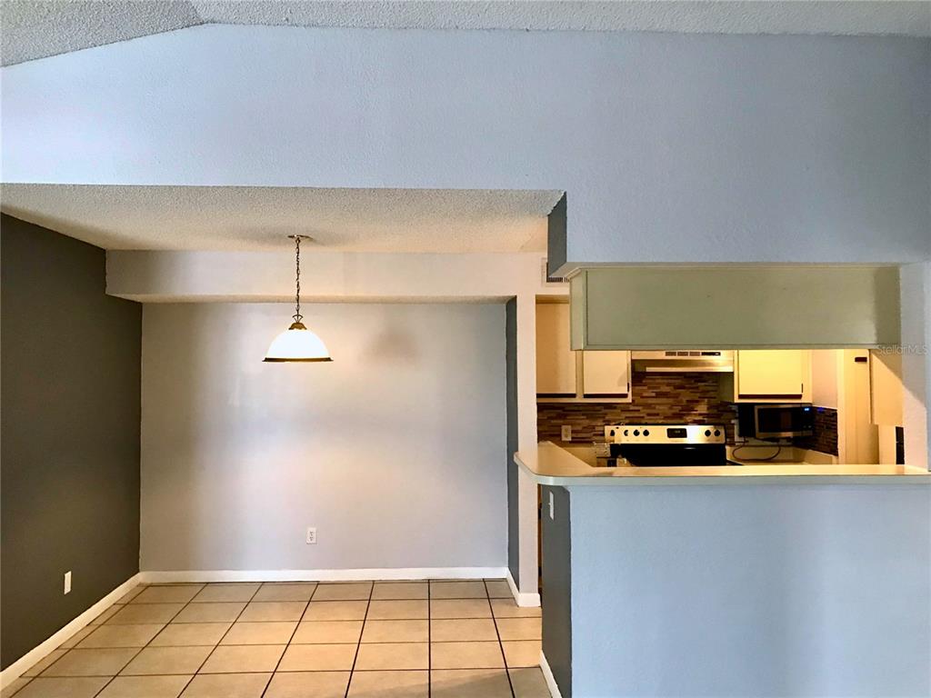 A dining area with tile floors and a pendant light sits adjacent to a kitchen — 4460 PERKINSHIRE LANE UNIT T206, ORLANDO, FL