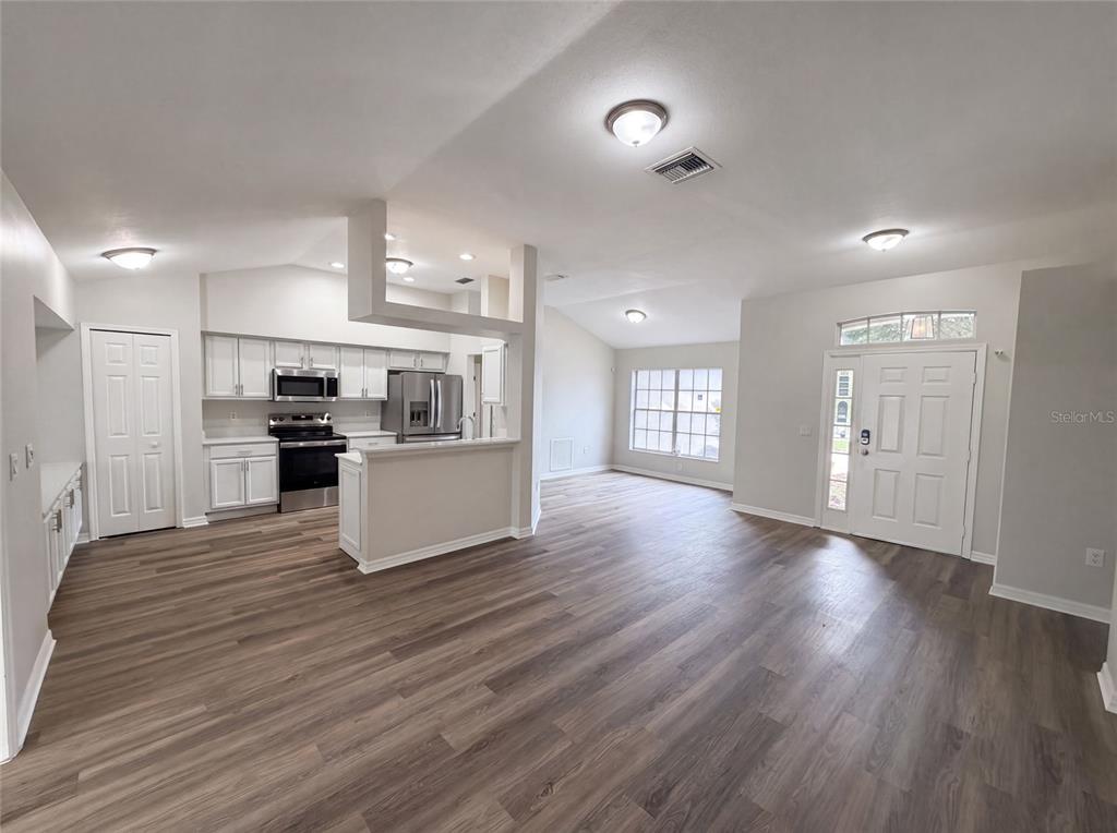 An open-concept living area features wood-look flooring, white cabinetry, and a kitchen with stainless appliances — 5217 PONCE DE LEON BOULEVARD, SEBRING, FL