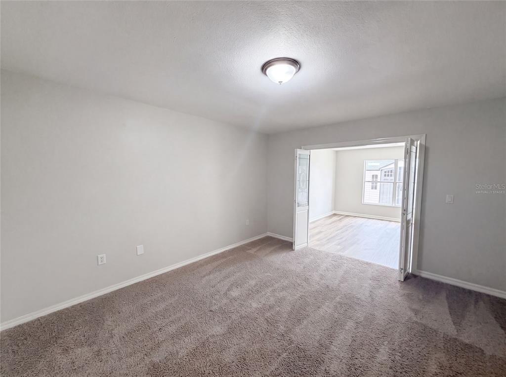 A carpeted room with light gray walls leads through French doors into a sunroom — 5217 PONCE DE LEON BOULEVARD, SEBRING, FL