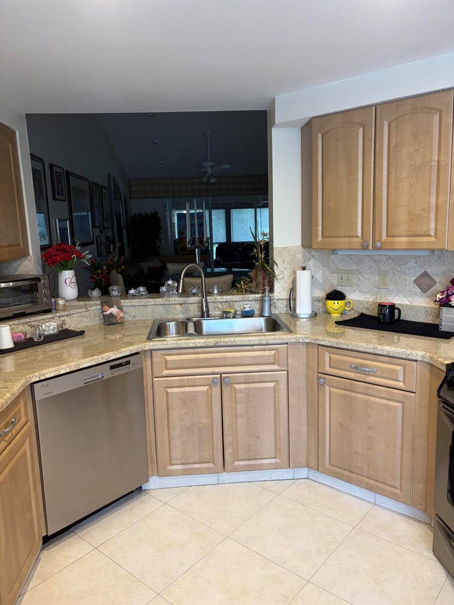 A kitchen features light wood cabinets, granite countertops, a stainless steel dishwasher, and a sink — 7254 Clunie Place # 15005, Delray Beach FL 33446, DELRAY BEACH, FL