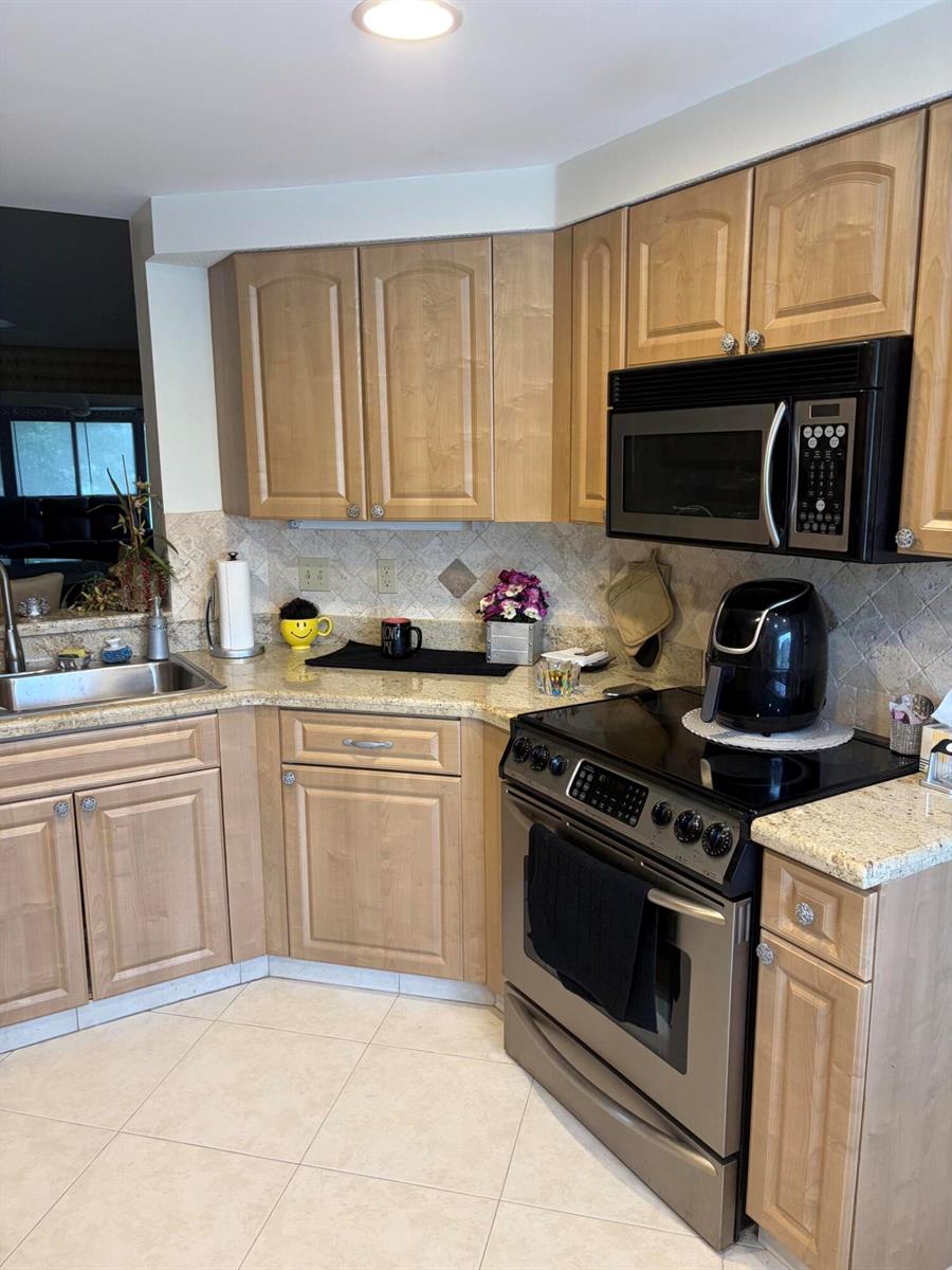A kitchen features light wood cabinets, granite countertops, stainless steel appliances, and a tiled backsplash — 7254 Clunie Place # 15005, Delray Beach FL 33446, DELRAY BEACH, FL