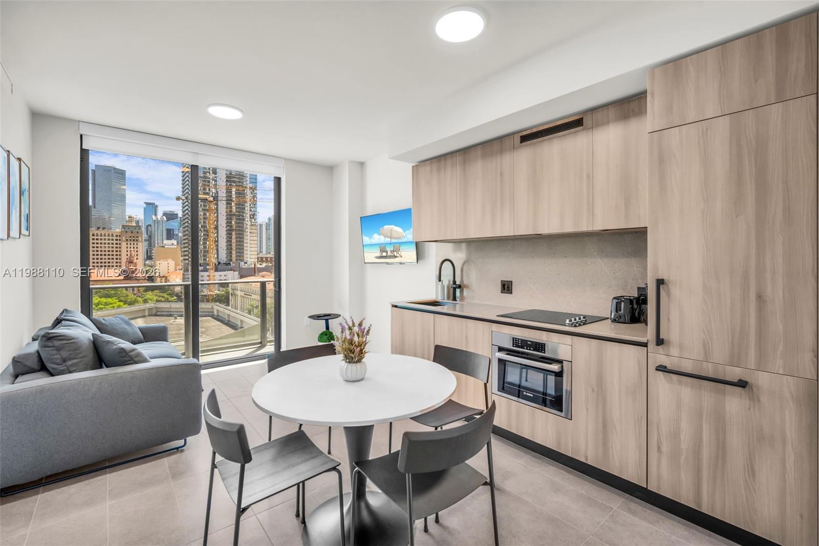 A modern studio apartment features a kitchenette, dining table, sofa, and a city view balcony — 121 NE 5th St # 902, Miami FL 33132, MIAMI, FL