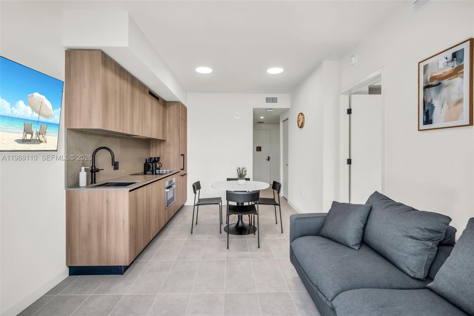 A modern studio apartment features a kitchenette with wood cabinetry, a dining table, and sofa — 121 NE 5th St # 902, Miami FL 33132, MIAMI, FL