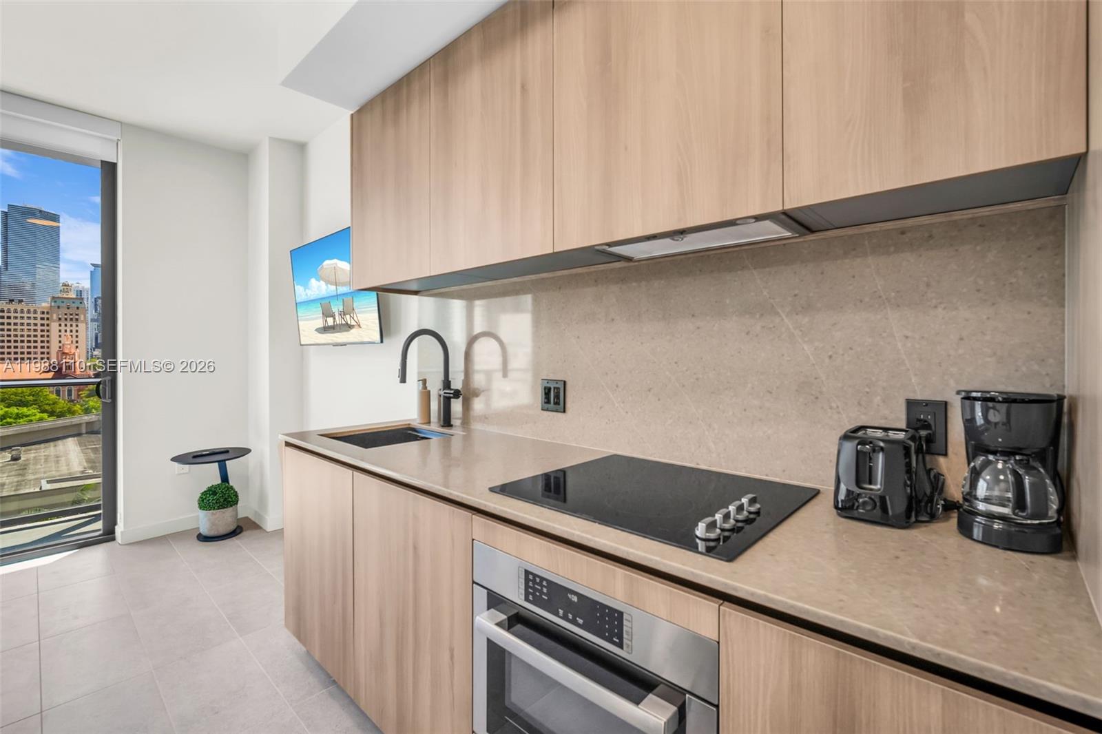 A modern kitchen features light wood cabinetry, a glass cooktop, and a view of city buildings — 121 NE 5th St # 902, Miami FL 33132, MIAMI, FL