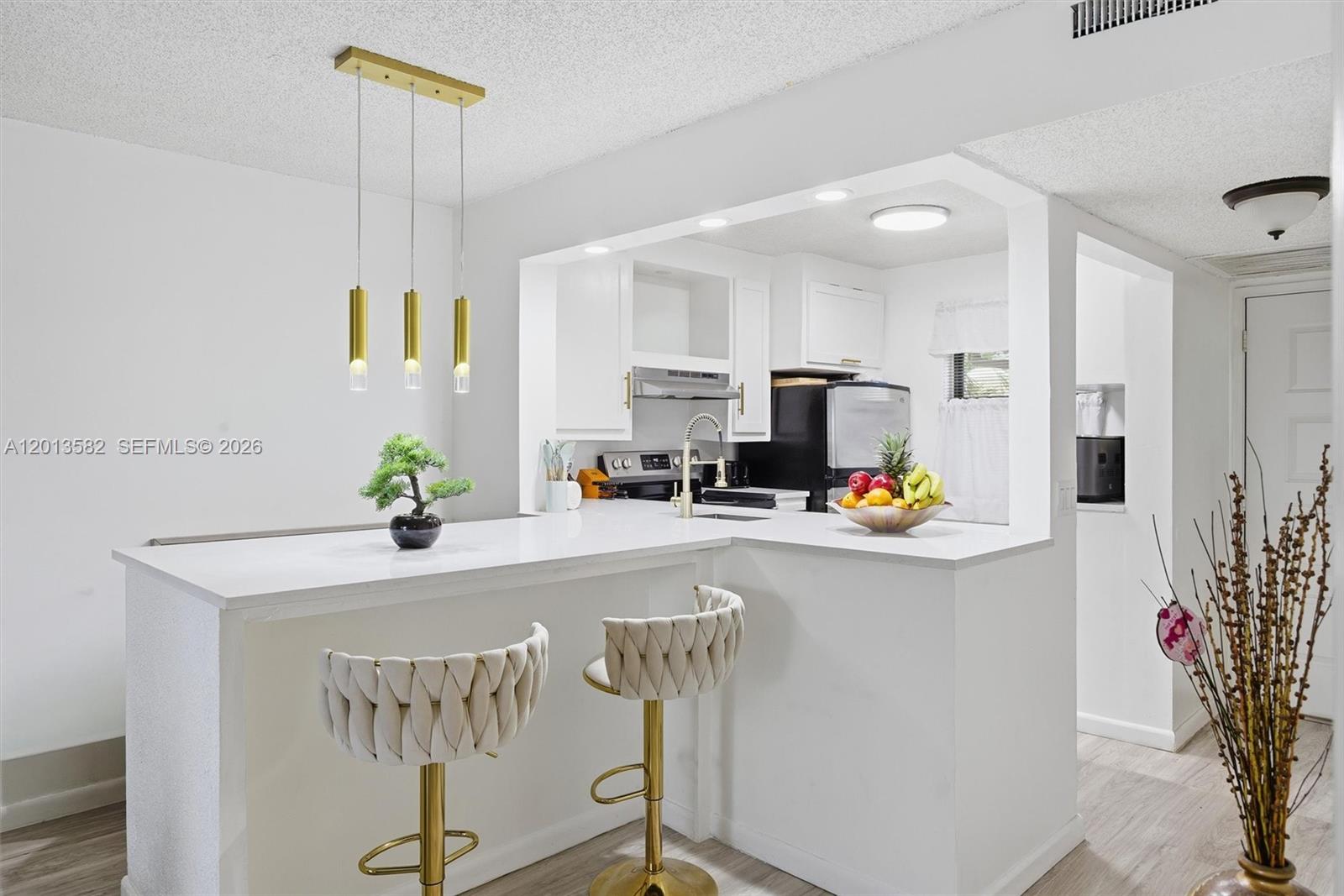 A white kitchen with stainless steel appliances opens to a living area with a balcony — 5501 Lakeside Dr # 204, Margate FL 33063, MARGATE, FL