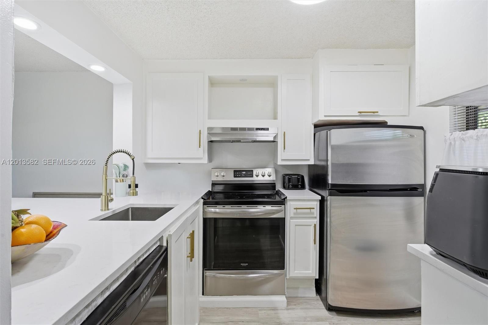 A white kitchen features a peninsula with a sink overlooking a living area — 5501 Lakeside Dr # 204, Margate FL 33063, MARGATE, FL