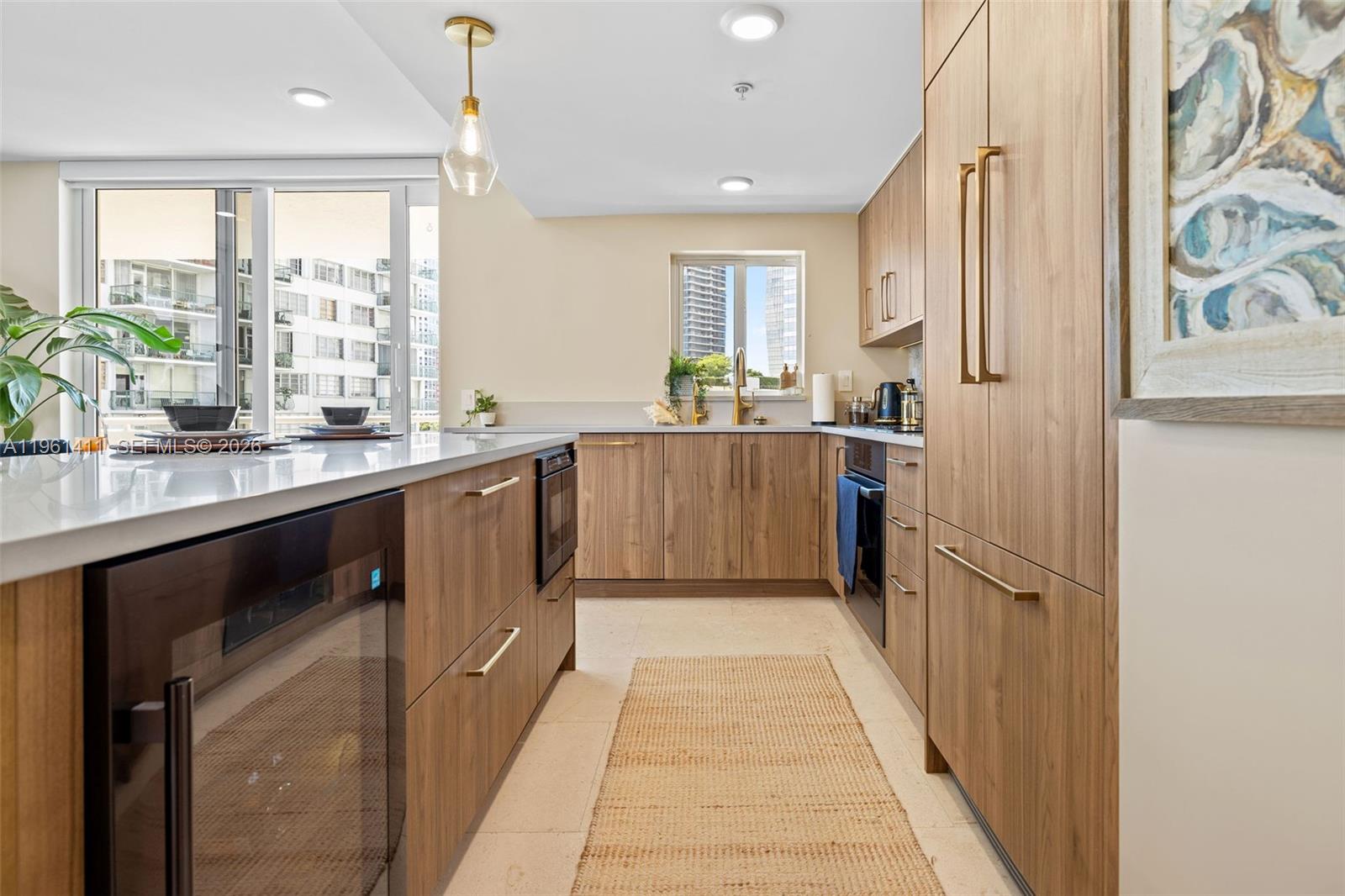 A modern kitchen features wood-grain cabinetry, gold hardware, and a white countertop island — 1402 Brickell Bay Dr # 603, Miami FL 33131, MIAMI, FL