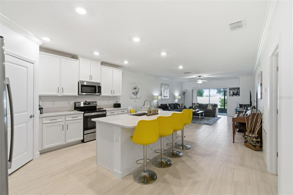 A modern kitchen with white cabinetry and a central island featuring three yellow bar stools — 31524 MAGNA GOLF LOOP, SAN ANTONIO, FL