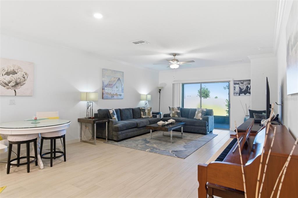 A living room with light tile floors, a blue sectional sofa, and a wooden piano — 31524 MAGNA GOLF LOOP, SAN ANTONIO, FL