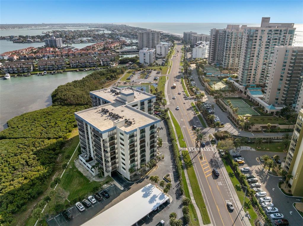 An aerial view shows a multi-story apartment building next to a road and coastal water — 1501 GULF BOULEVARD UNIT 603, CLEARWATER BEACH, FL