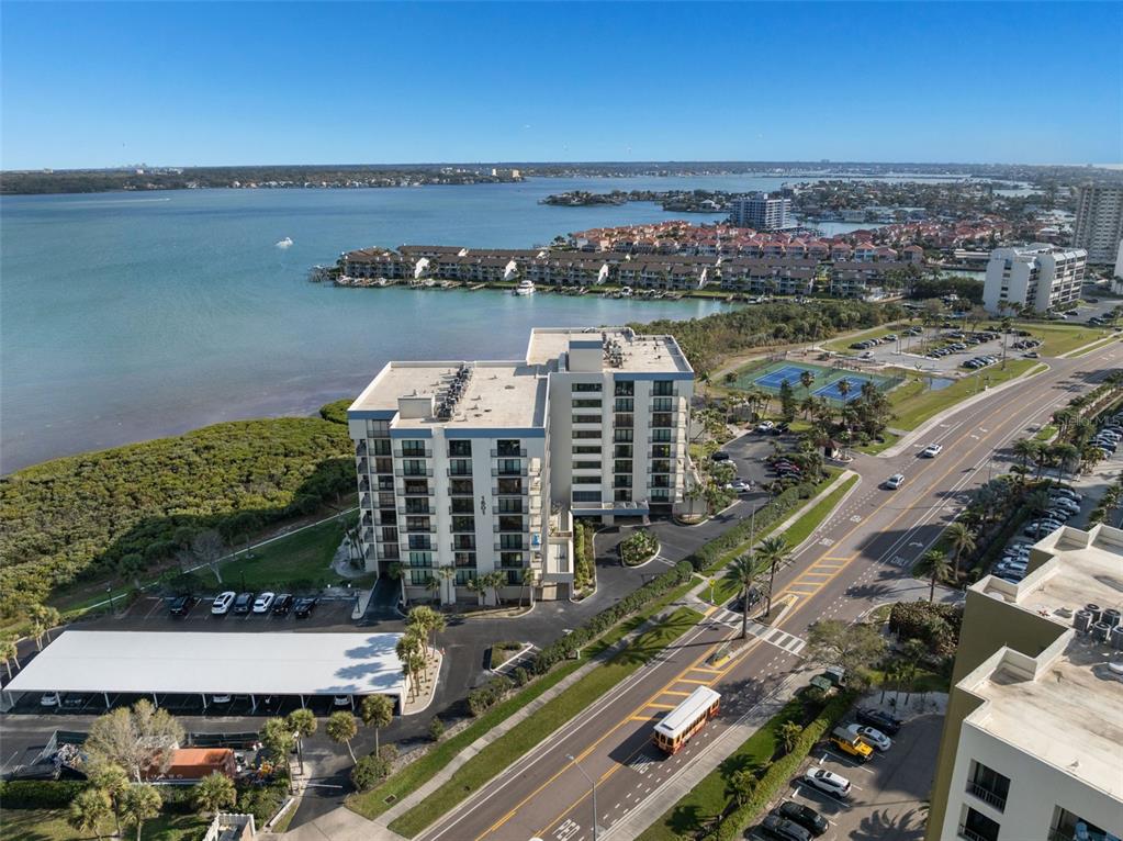 An aerial view shows a multi-story waterfront condominium building, parking areas, and a nearby road — 1501 GULF BOULEVARD UNIT 603, CLEARWATER BEACH, FL