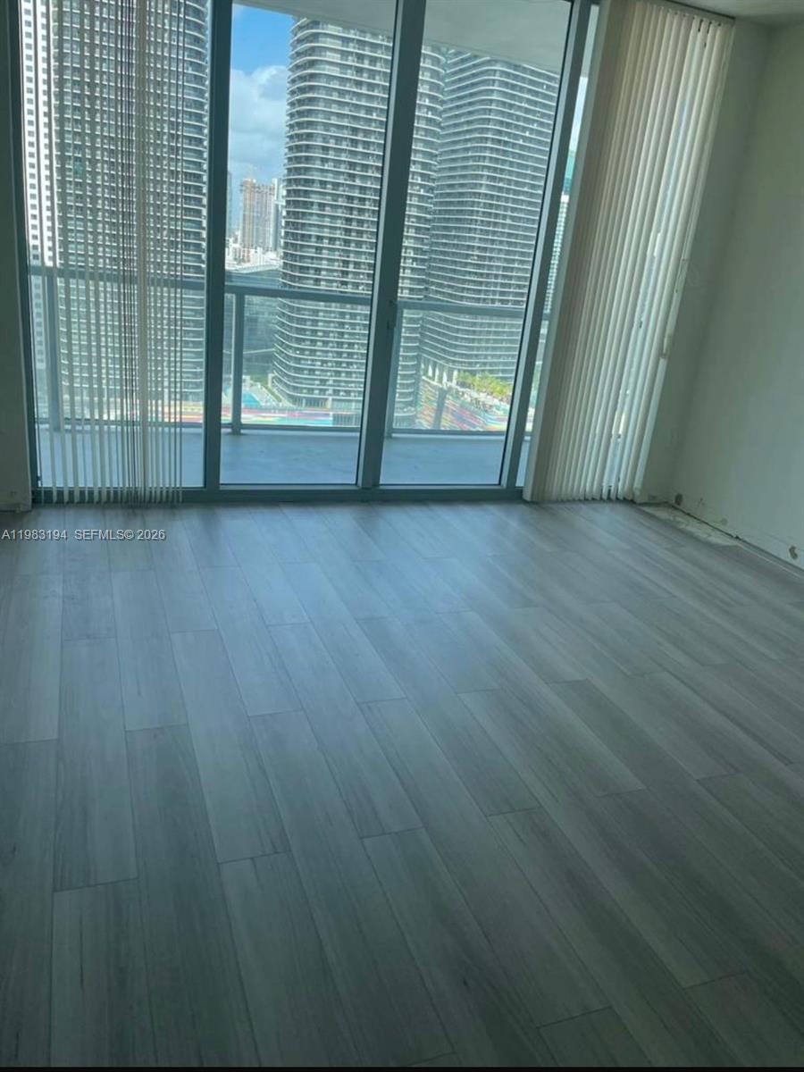 An empty room features light-colored wood-look flooring and floor-to-ceiling windows overlooking city skyscrapers — 1111 SW 1st Ave, Miami FL 33130, MIAMI, FL