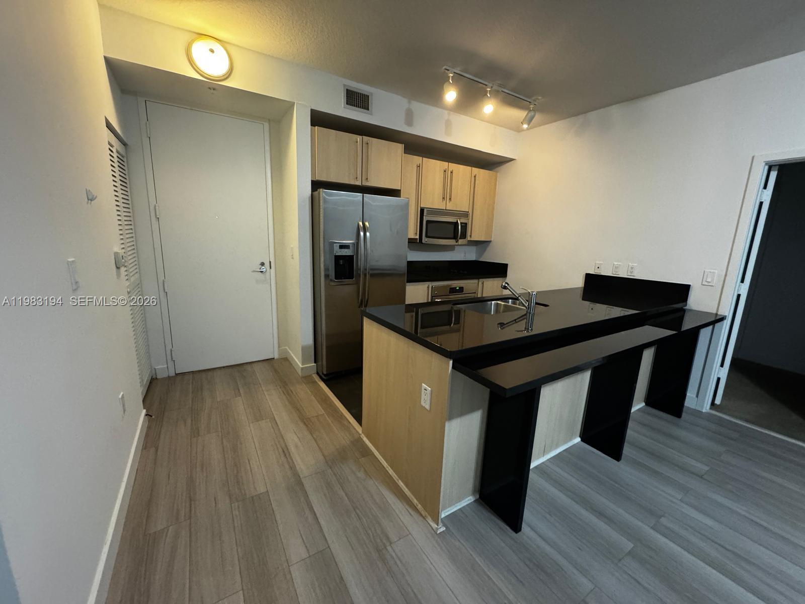 A kitchen features light wood cabinets, stainless steel appliances, and a black countertop island — 1111 SW 1st Ave, Miami FL 33130, MIAMI, FL