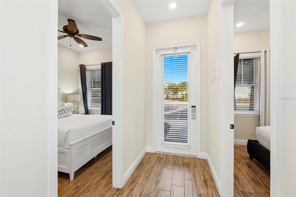 A hallway with wood-look tile floors leads to an exterior door between two bedrooms — 8098 KNEE DEEP ROAD, KISSIMMEE, FL