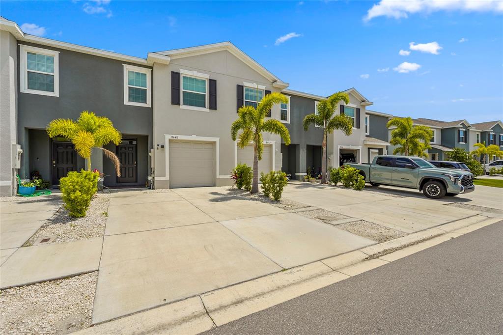 A row of two-story townhouses with attached garages and concrete driveways under a blue sky — 8652 MILESTONE DRIVE, SARASOTA, FL