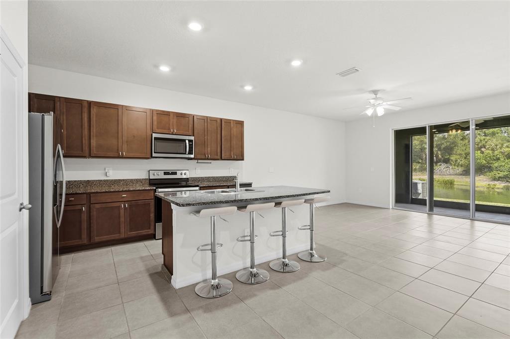 A kitchen with dark wood cabinets, granite countertops, and an island with four bar stools — 8652 MILESTONE DRIVE, SARASOTA, FL