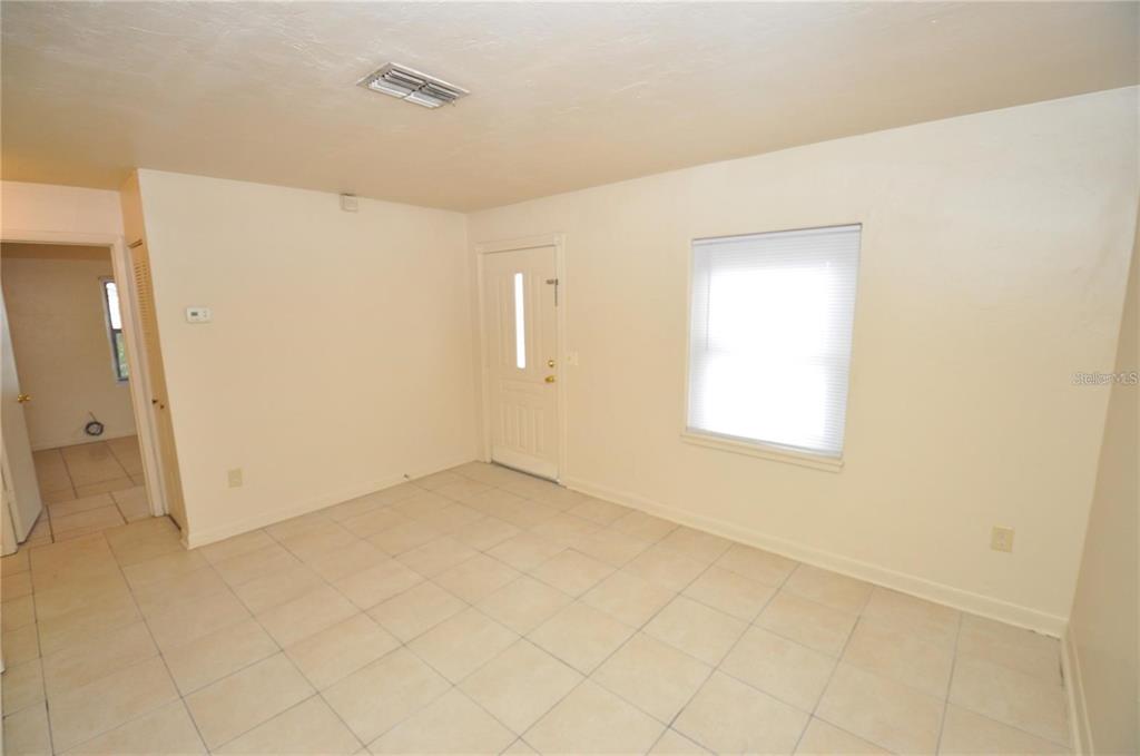 An empty room features light-colored floor tiles, beige walls, a front door, and a window — 730 28TH STREET NW, WINTER HAVEN, FL
