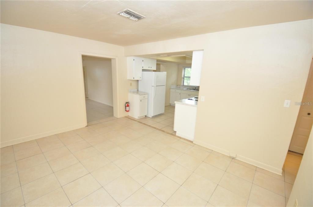 An interior view of a tiled dining area leading into a kitchen with white appliances — 730 28TH STREET NW, WINTER HAVEN, FL