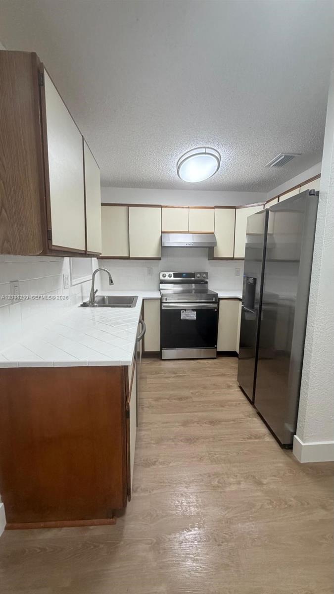 A kitchen features white tiled countertops, wood-trimmed cabinets, and stainless steel appliances — 2580 NW 62nd Ave, Margate FL 33063, MARGATE, FL