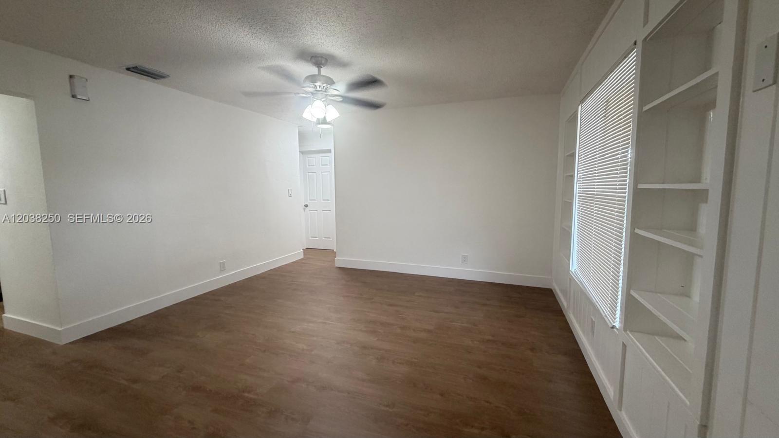 An empty room features white walls, wood-look flooring, a ceiling fan, and built-in shelving — 2580 NW 62nd Ave, Margate FL 33063, MARGATE, FL