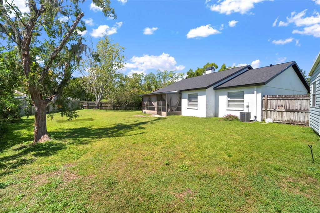 A backyard view of a single-story house with a screened porch and a wooden fence — 4613 N COUNTRY HILLS COURT, PLANT CITY, FL