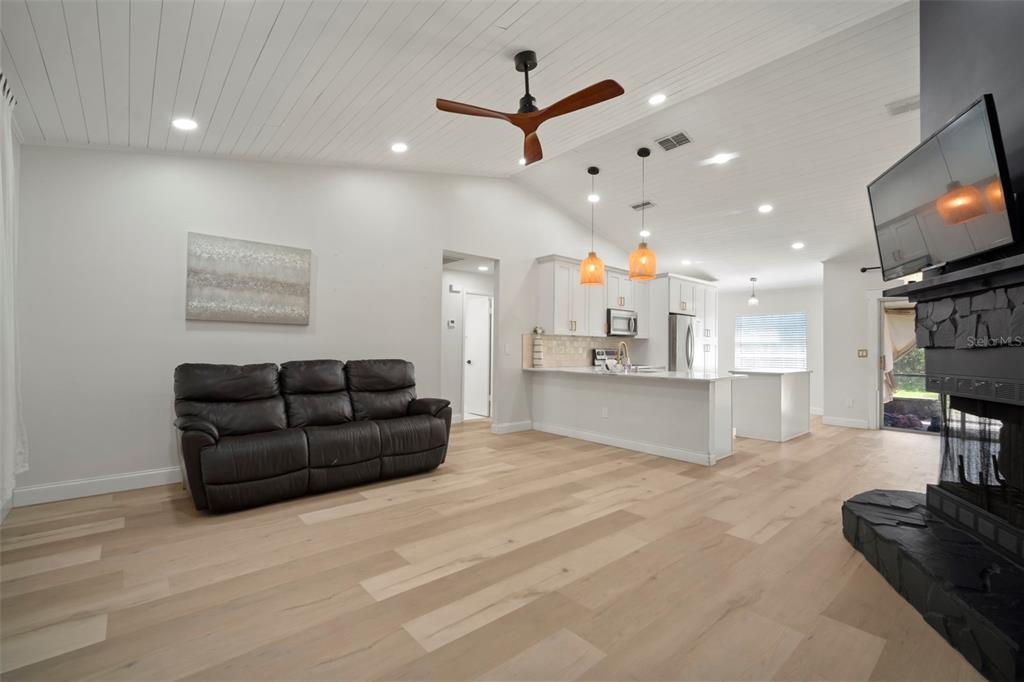A living room with light wood flooring, a dark leather sofa, and an open kitchen — 4613 N COUNTRY HILLS COURT, PLANT CITY, FL
