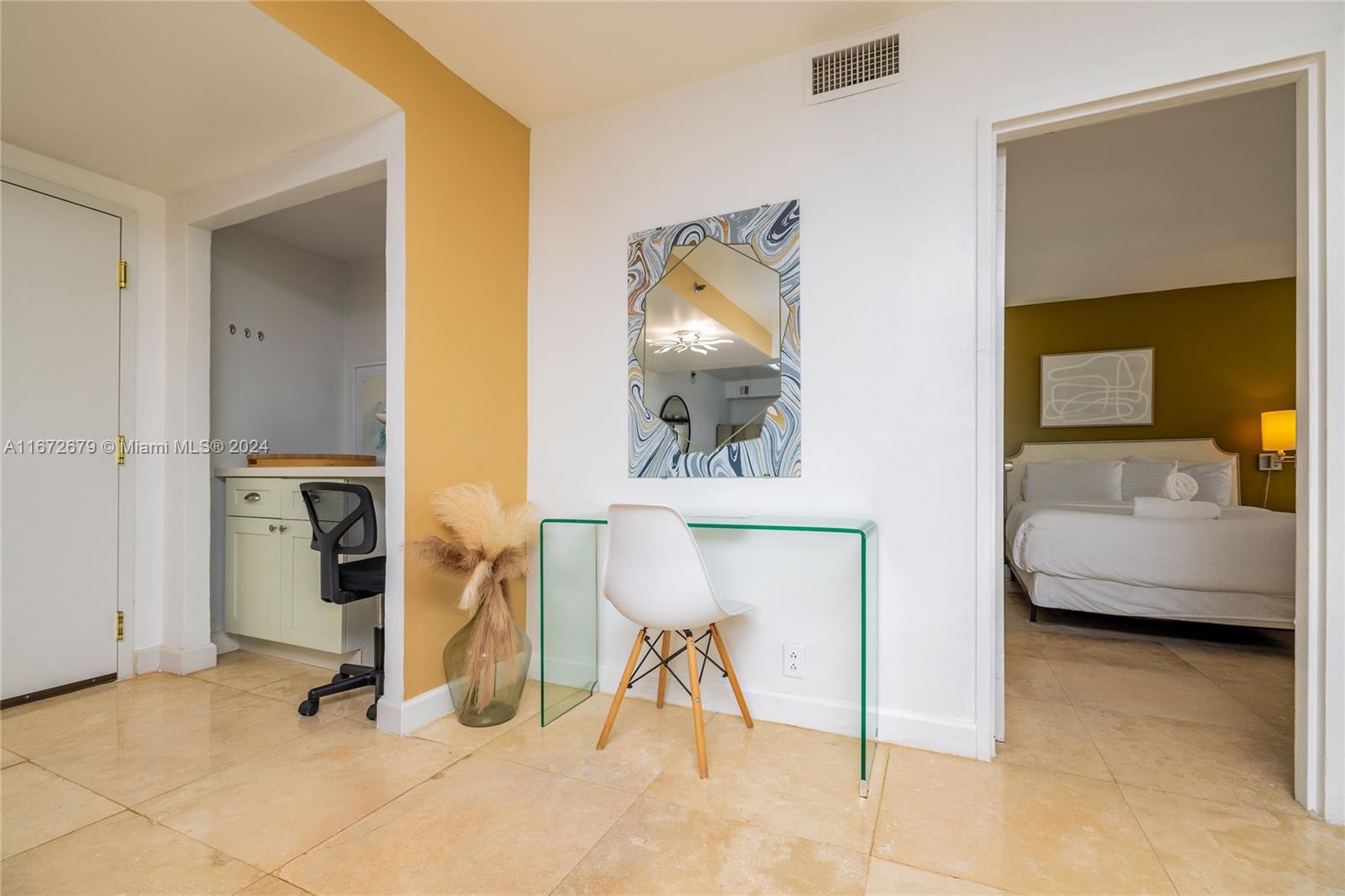 A glass desk and chair sit between a kitchen area and a bedroom doorway — 5225 Collins Ave # 1114, Miami Beach FL 33140, MIAMI BEACH, FL