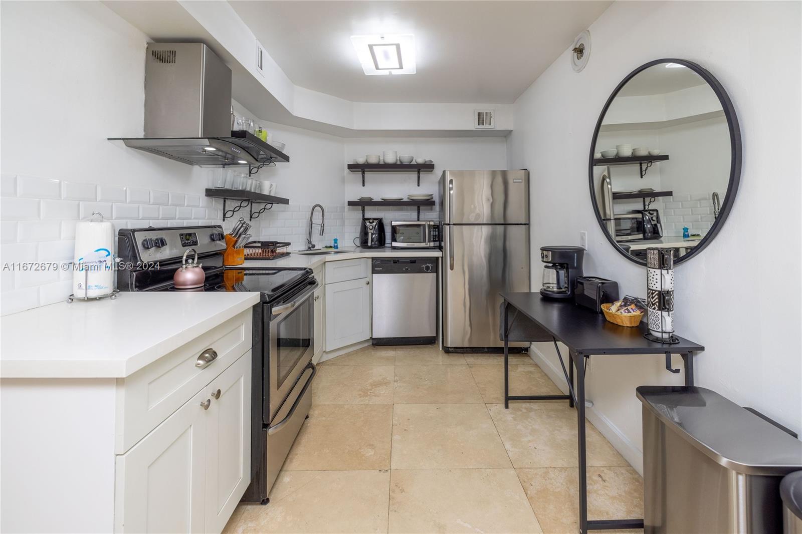 A kitchen features white cabinets, stainless steel appliances, open shelving, and a round wall mirror — 5225 Collins Ave # 1114, Miami Beach FL 33140, MIAMI BEACH, FL