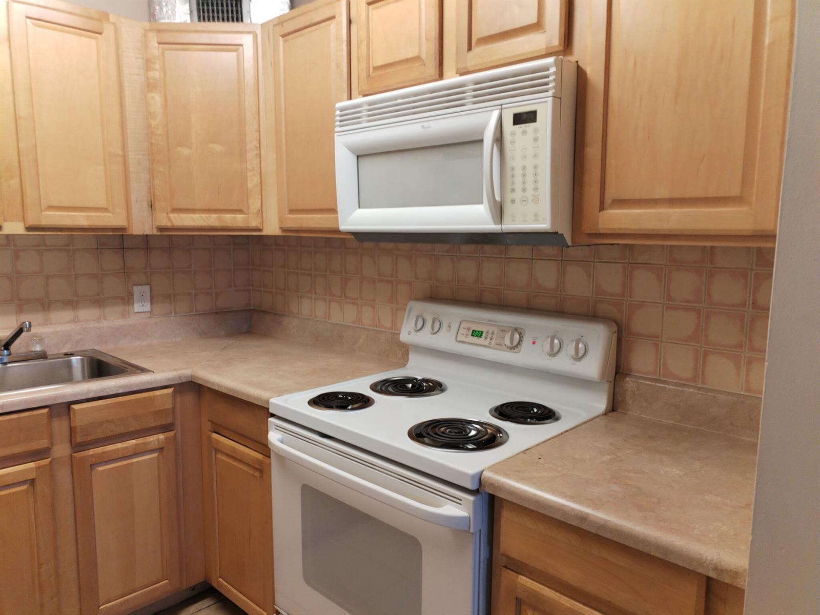 A kitchen features light wood cabinets, a white stove, a microwave, and tan tiled backsplash — 420 S B Street # A4, FL 33460, FL