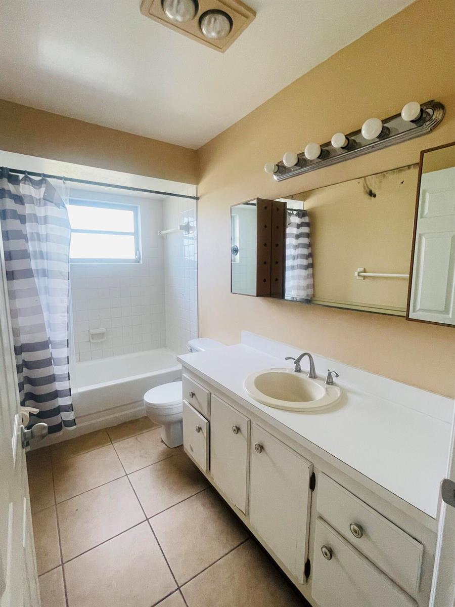A bathroom features a vanity with a white countertop, a mirror, and a shower-tub combo — 420 S B Street # A4, FL 33460, FL